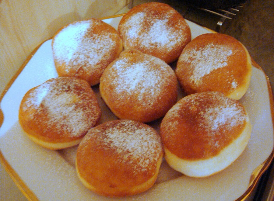 A plate of round golden gogoși dusted with powdered sugar