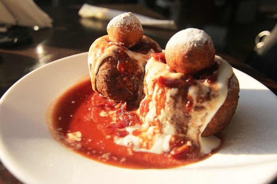 Papanași in a pool of sour cherry sauce with cream